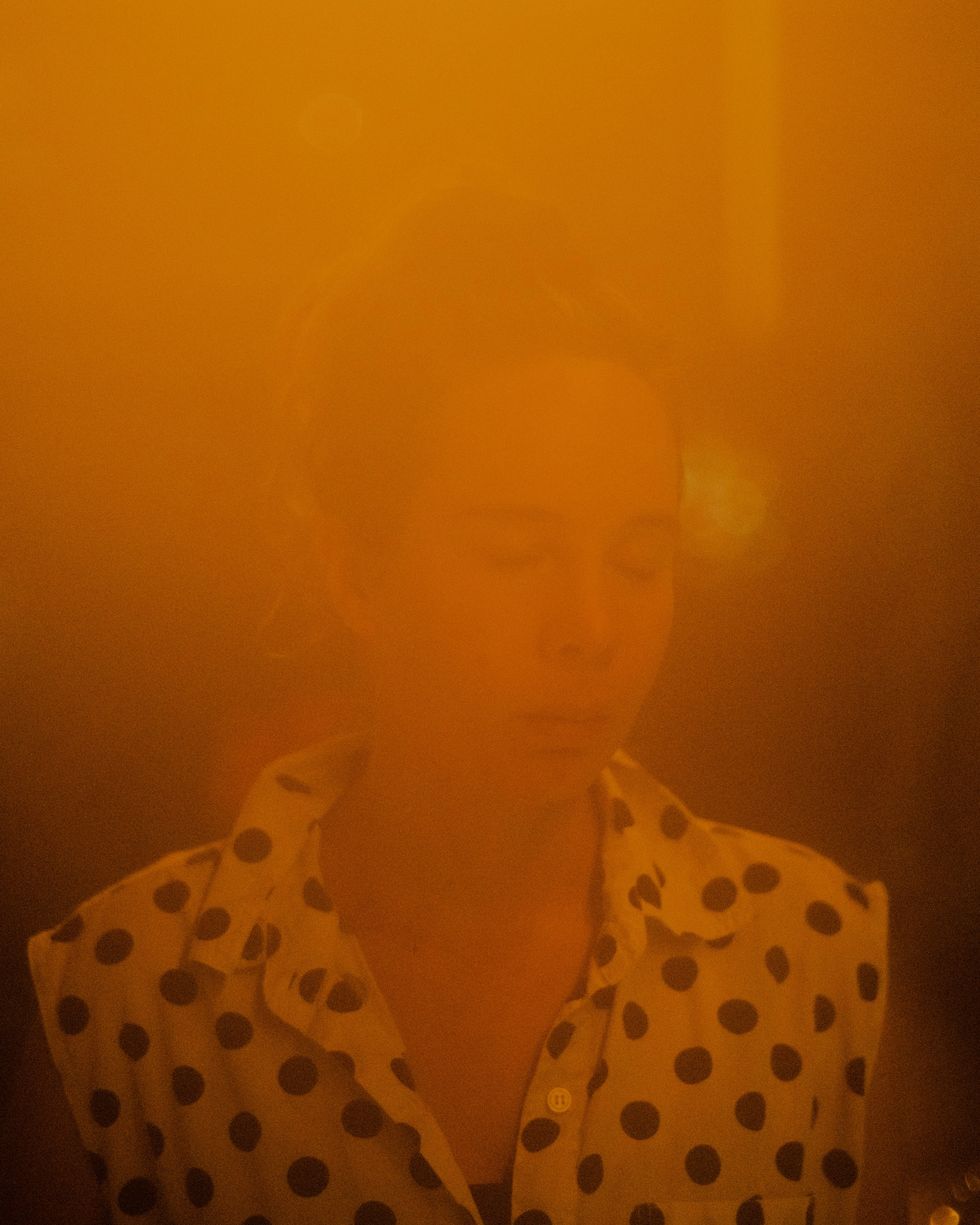 Paradise by Daniel Dorsa, photographed by Daniel Dorsa — A person in a polka-dot shirt, the face washed in orange light.