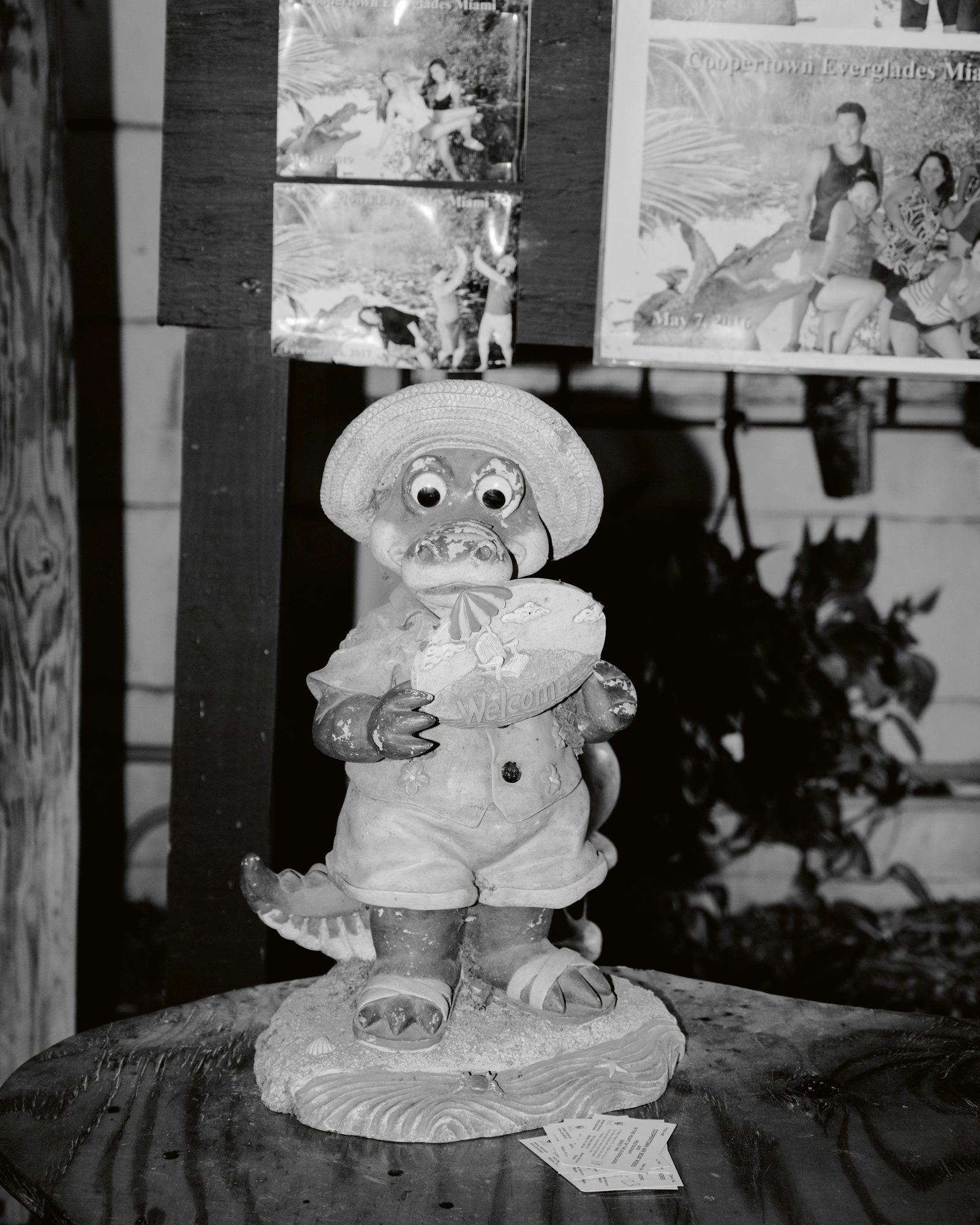 Paradise by Daniel Dorsa, photographed by Daniel Dorsa — In black and white, a figurine in a hat holding a plate, with photographs pinned to the wall behind.