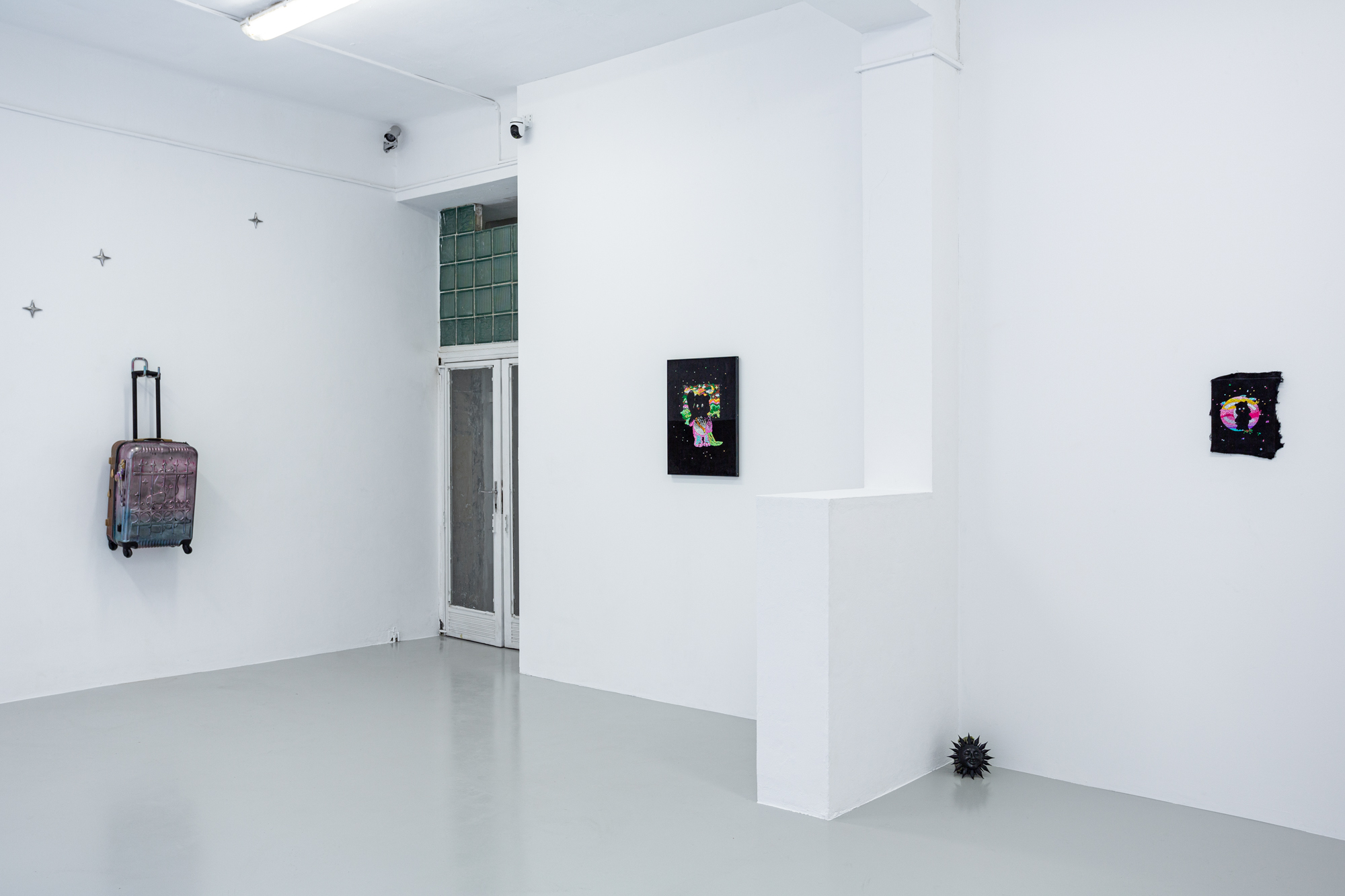 Ready or Not by Ondřej Kotrč, photographed by Monika Rygálová — Room view with the hanging suitcase under three star shapes, a doorway, two works on black grounds and a black sun on the floor.