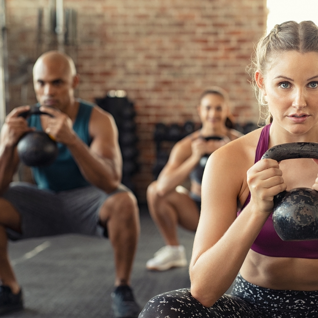 People performing kettlebell squats during a group fitness workout in a gym