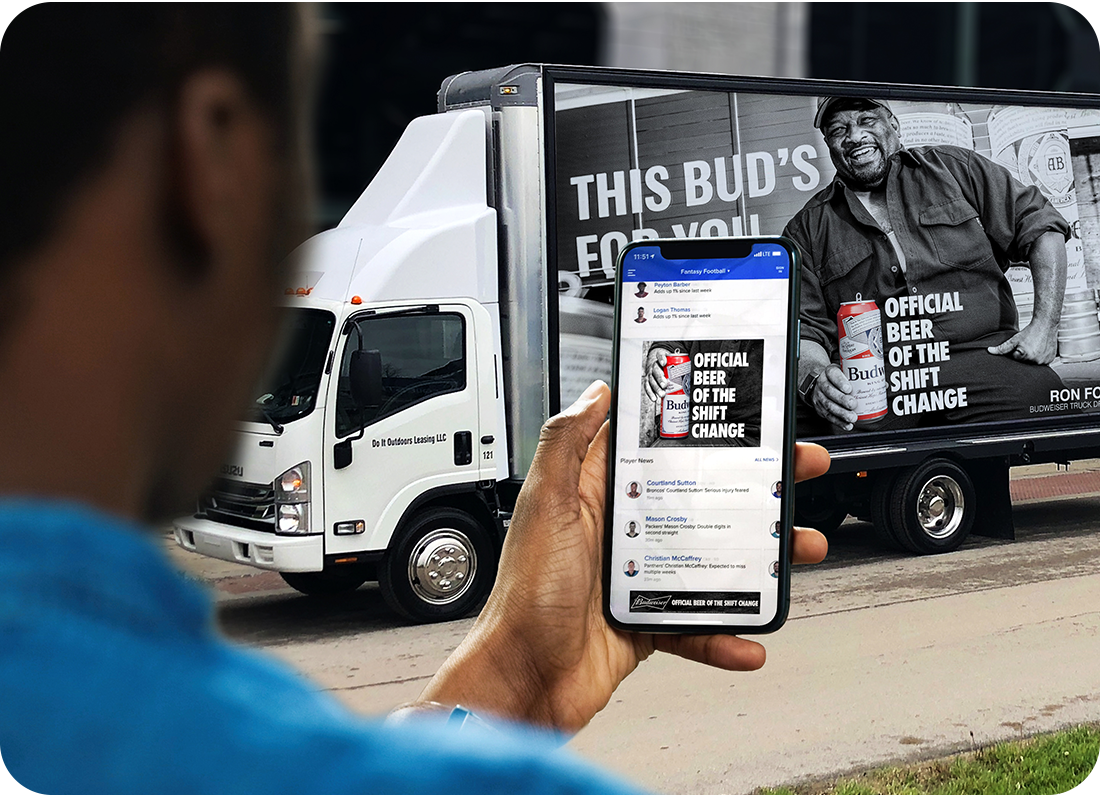 Man looking at phone on the street with an ad that is on a passing vehicle. 