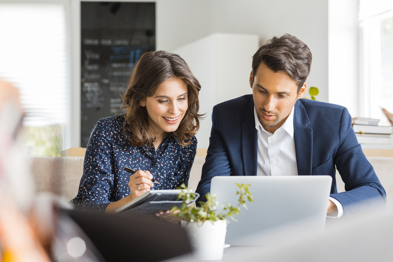 man-and-woman-in-library-work-room-consulting-on-work-with-laptop-and-notepad-at-table