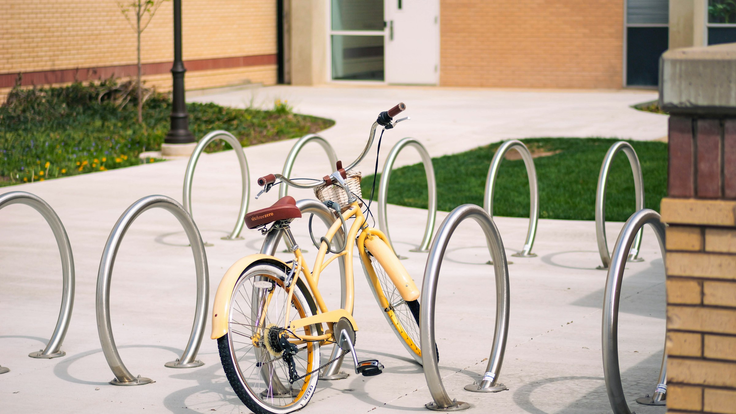 A yellow bicycle parked at curved metal bike racks outside a building