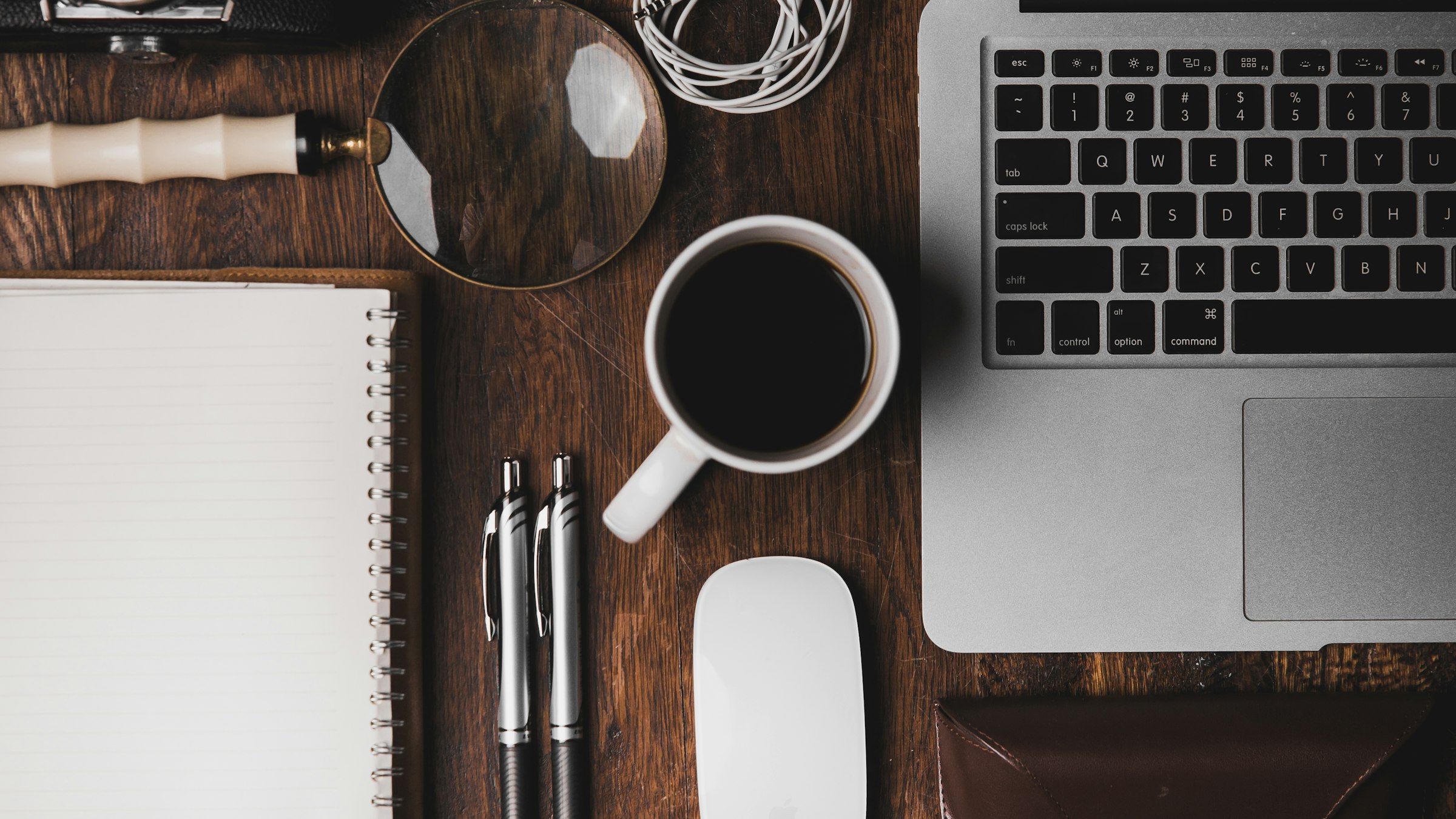 A desk with a notebook, coffee and a keyboard