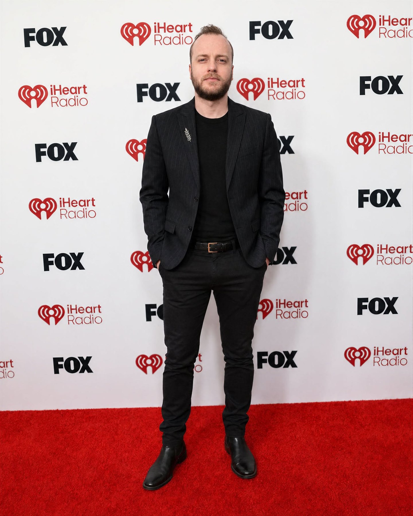Valev Laube in a dark pinstripe suit on the red carpet at an iHeartRadio and FOX step-and-repeat
