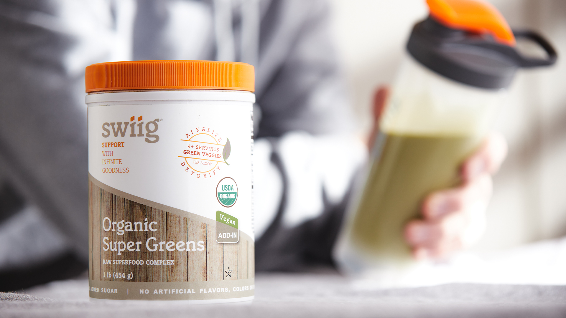 Person holding a swiig shaker bottle with a protein shake in it next to a counter with swiig organic super greens
