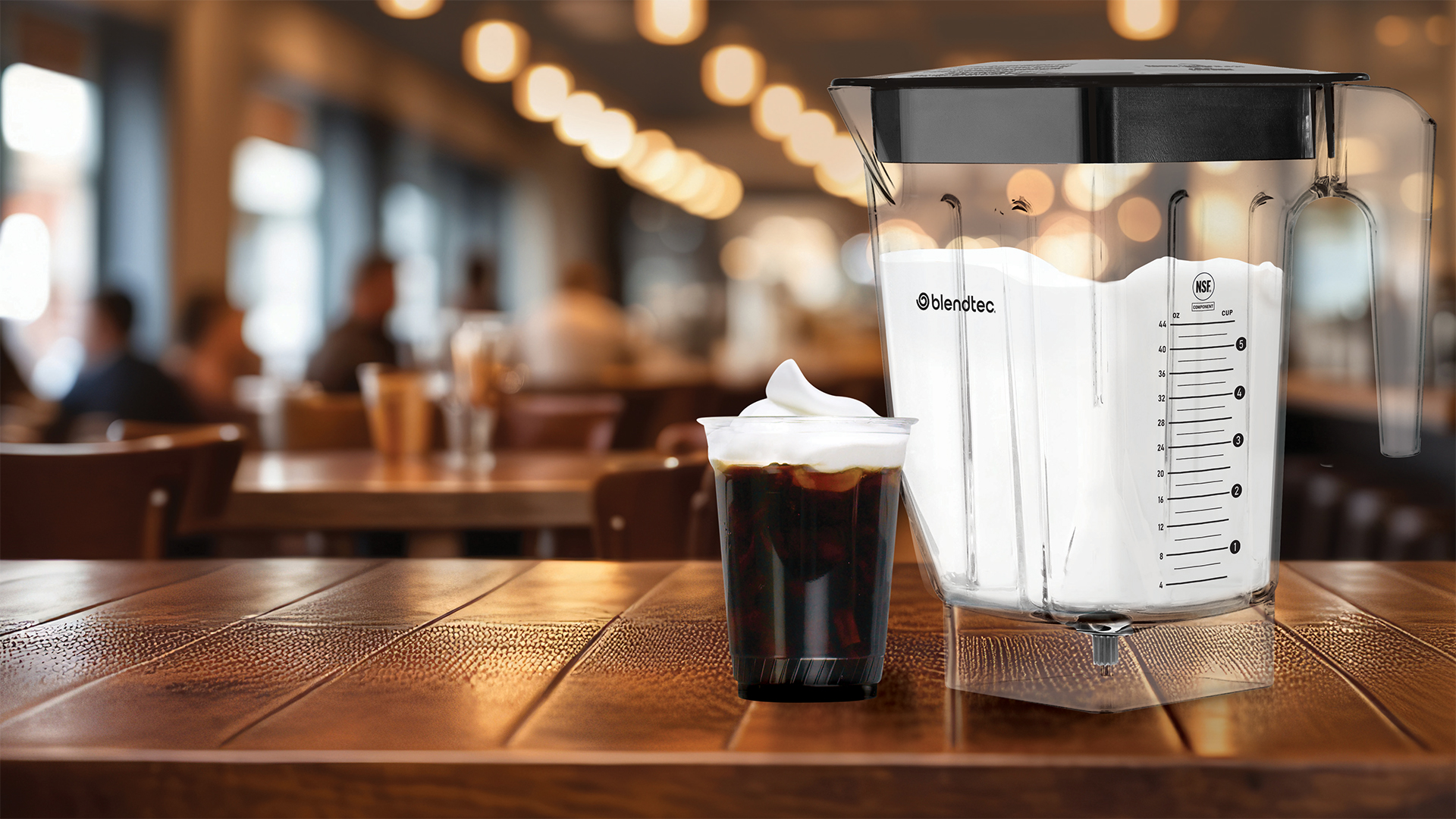 Cold Brew Coffee with Protein Cold Foam ontop on a wooden counter in a smoothie bar next to a blender of protein cold foam