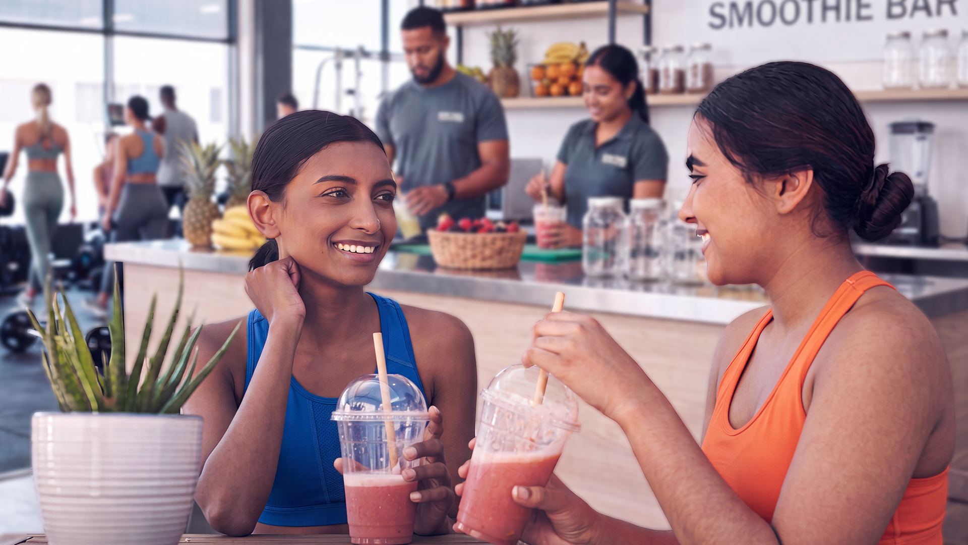 Two girls sitting at a table at the gym juice bar drinking smoothies