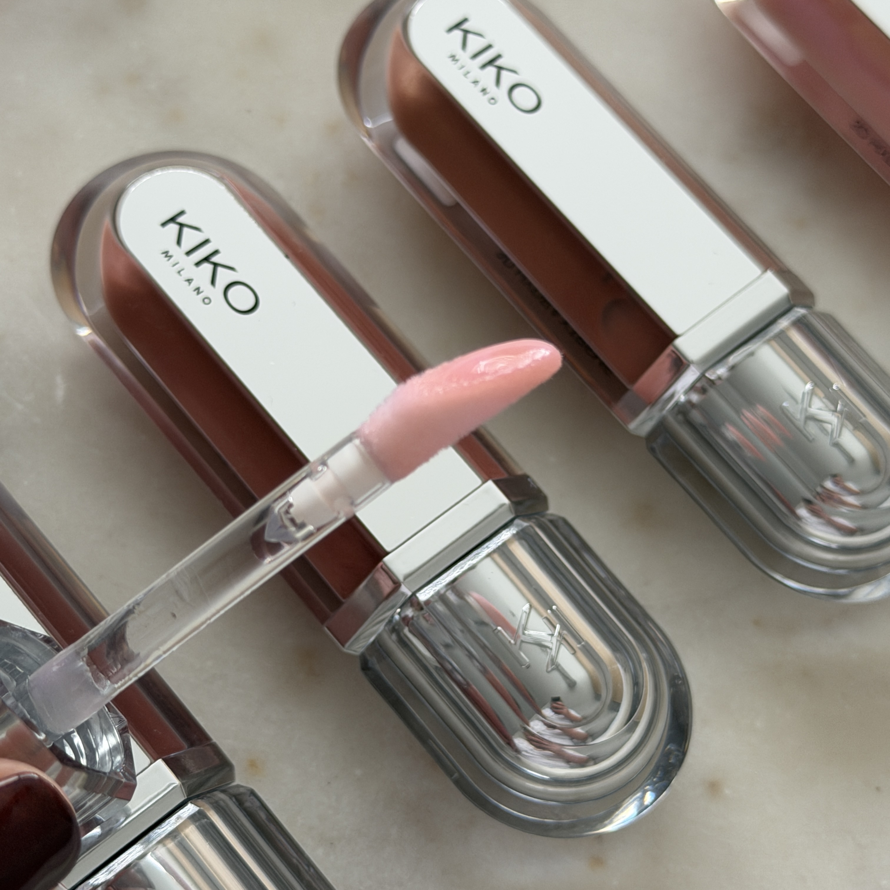 Close up of lip gloss applicator with pink gloss on it