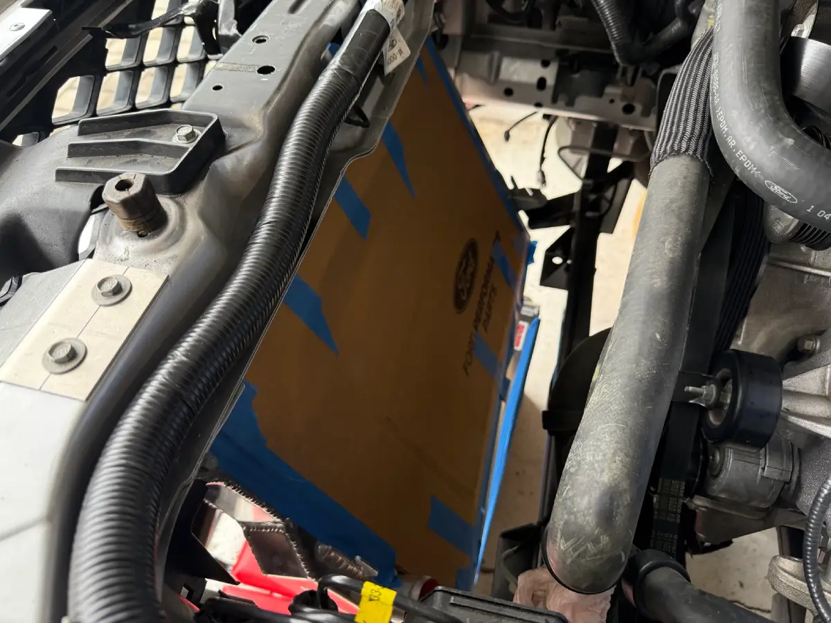 Side view of the forward-leaned radiator in an S197 Mustang, with a custom upper bracket extension and cardboard protecting the core.