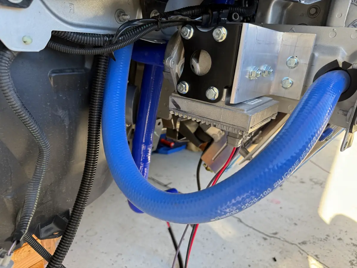 EMP intercooler pump on a custom aluminum frame bracket, with blue silicone hose routed through a protected frame opening.