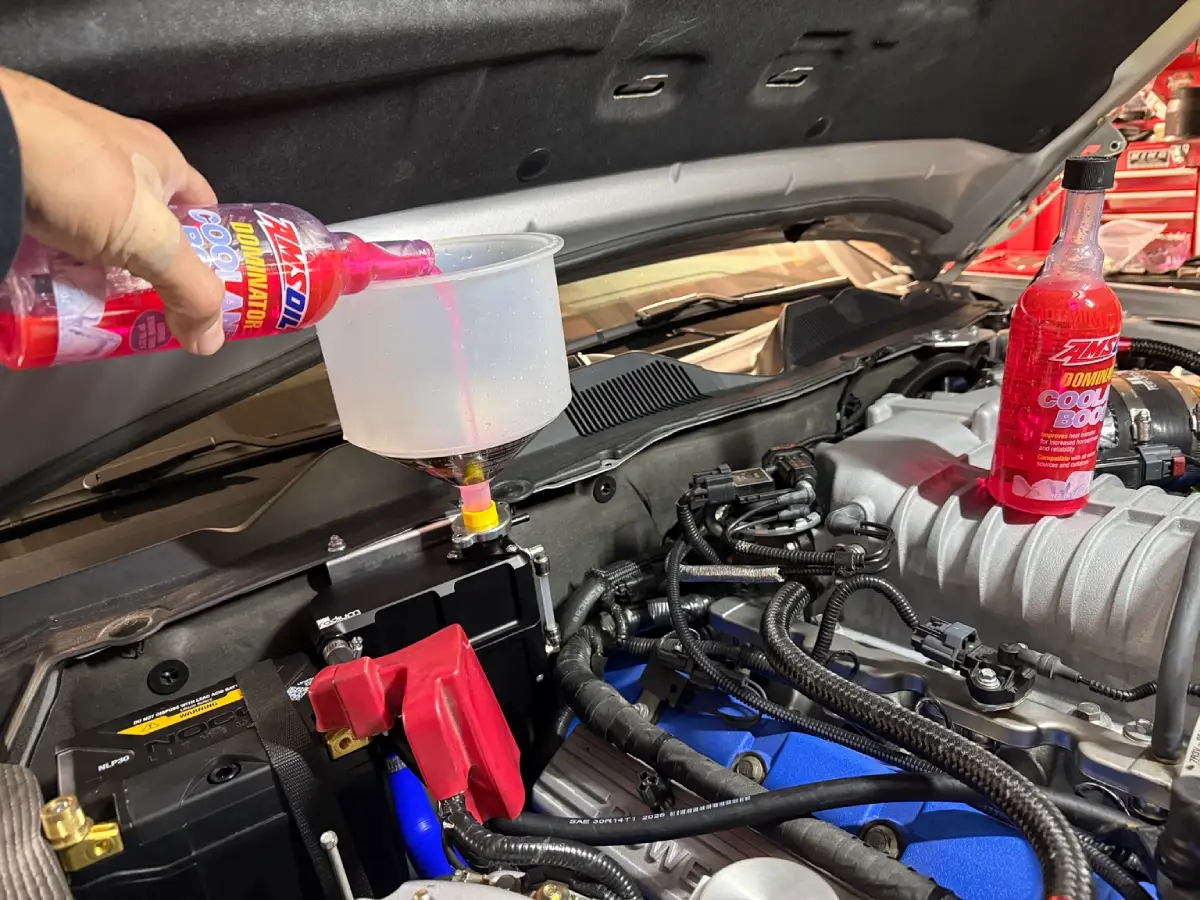 Pouring AMSOIL Dominator Coolant Boost into a funnel on the GT500's firewall-mounted Radium coolant reservoir.