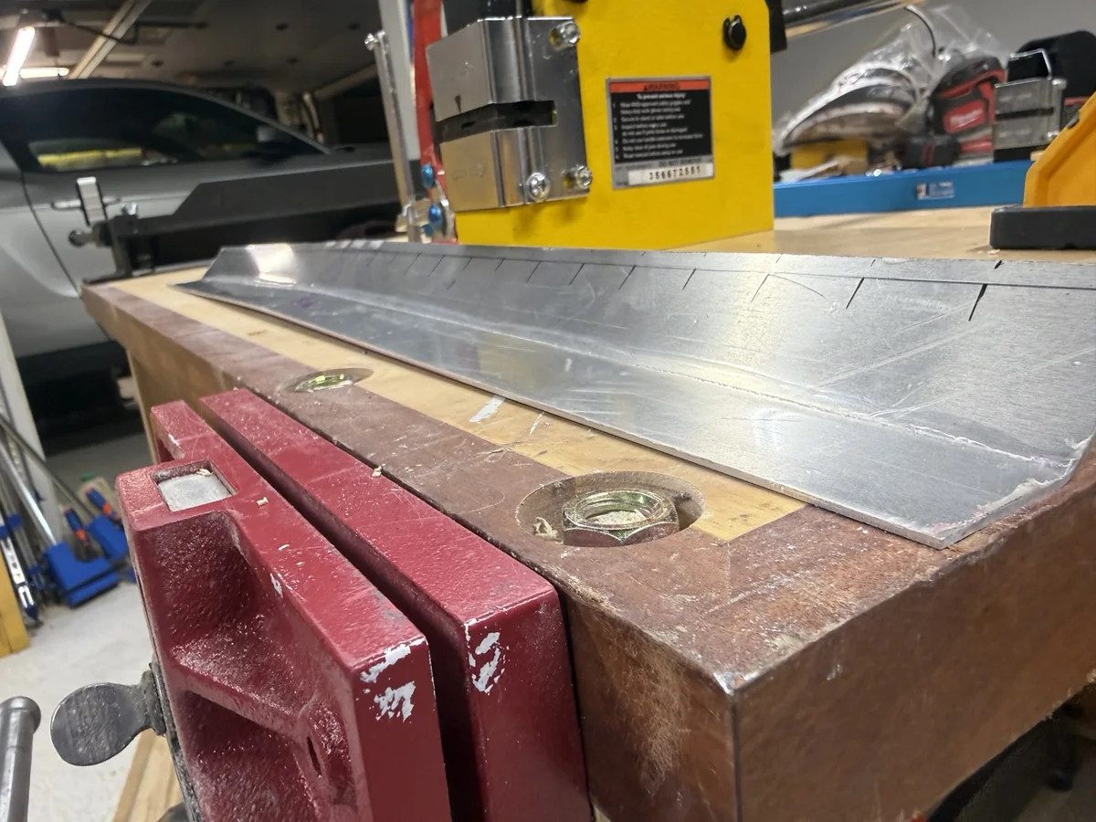 Layout marks along the upper edge of an aluminum hood gurney flap beside a metal stretcher.