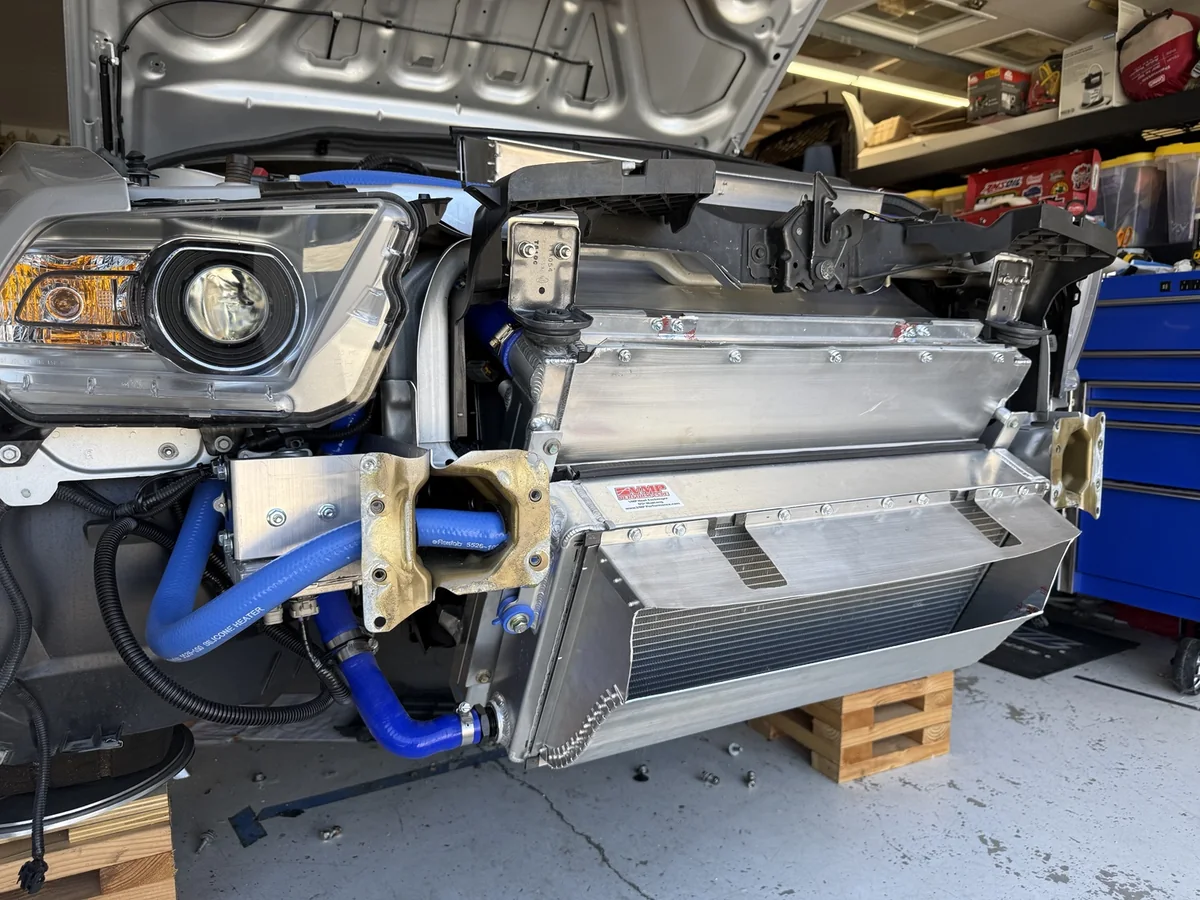 Angled view of the installed GT500 aluminum inlet duct, VMP heat exchanger, radiator panels, and blue coolant hoses.