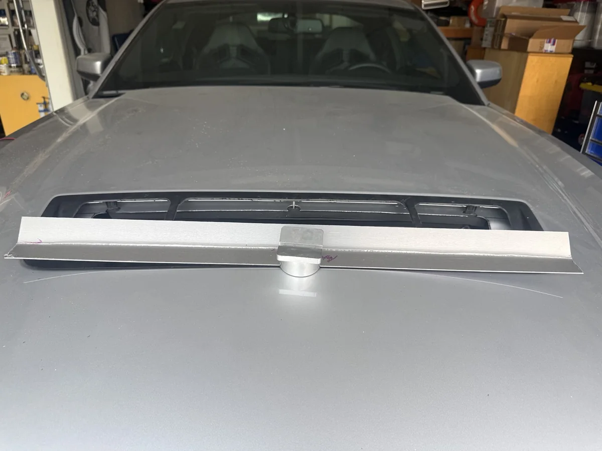 Initial test fit of a straight bent aluminum gurney flap across the curved GT500 hood vent.