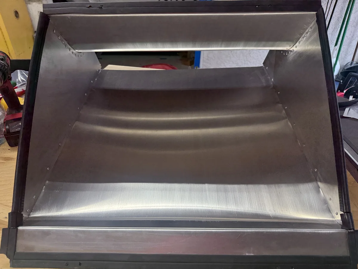 Inside the aluminum radiator outlet duct, showing curved panels, internal rivet heads, and edge trim.