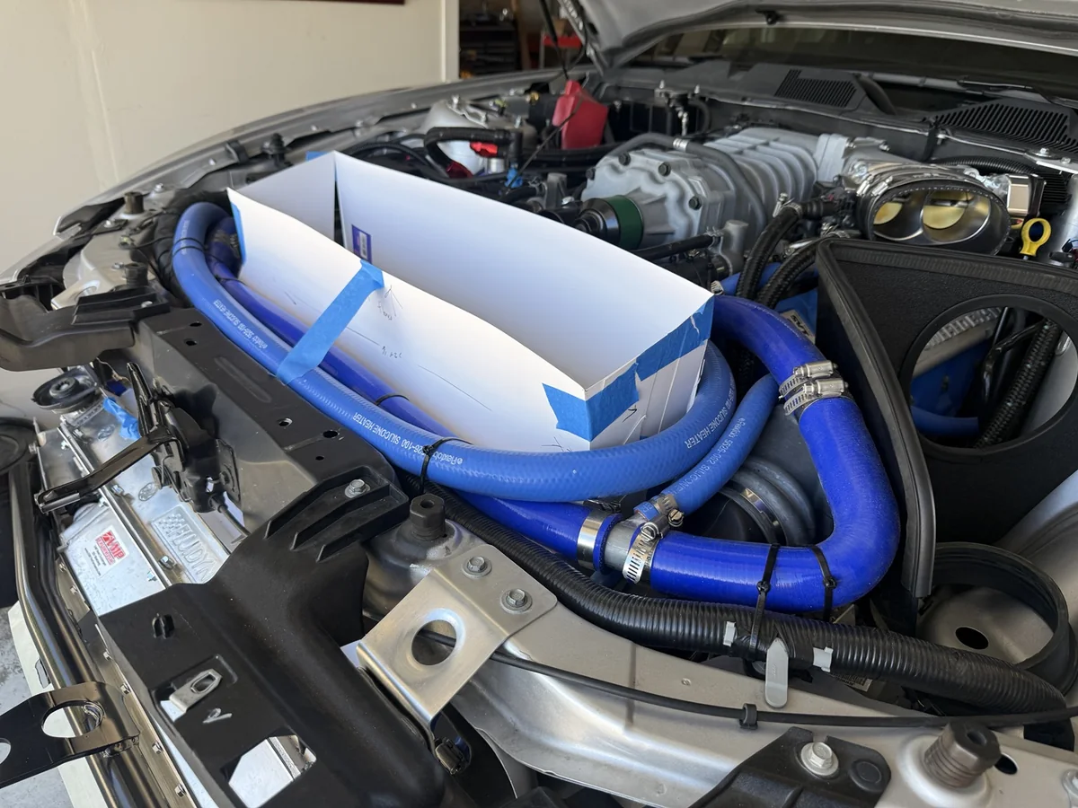 Poster-board radiator outlet template fitted among the blue coolant hoses in a GT500 engine bay.