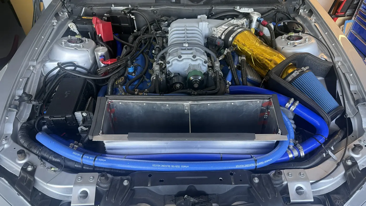 Completed aluminum radiator outlet duct and blue coolant hoses in the engine bay of my 2012 Shelby GT500.