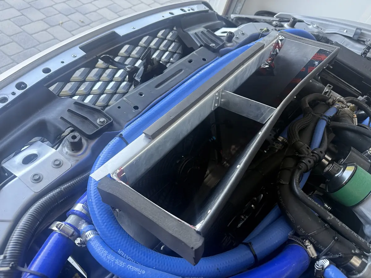Installed GT500 radiator outlet duct showing the center tie, curved rear edge, foam sealing strips, and taped corner seams.