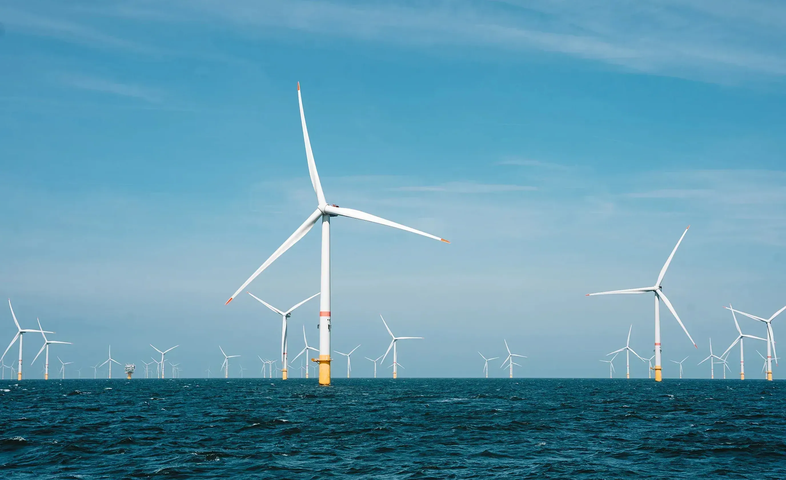 Offshore wind farm with multiple wind turbines standing in the ocean under a clear blue sky.