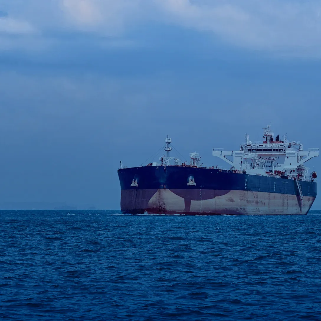 Large cargo ship sailing on a calm ocean under a cloudy blue sky.