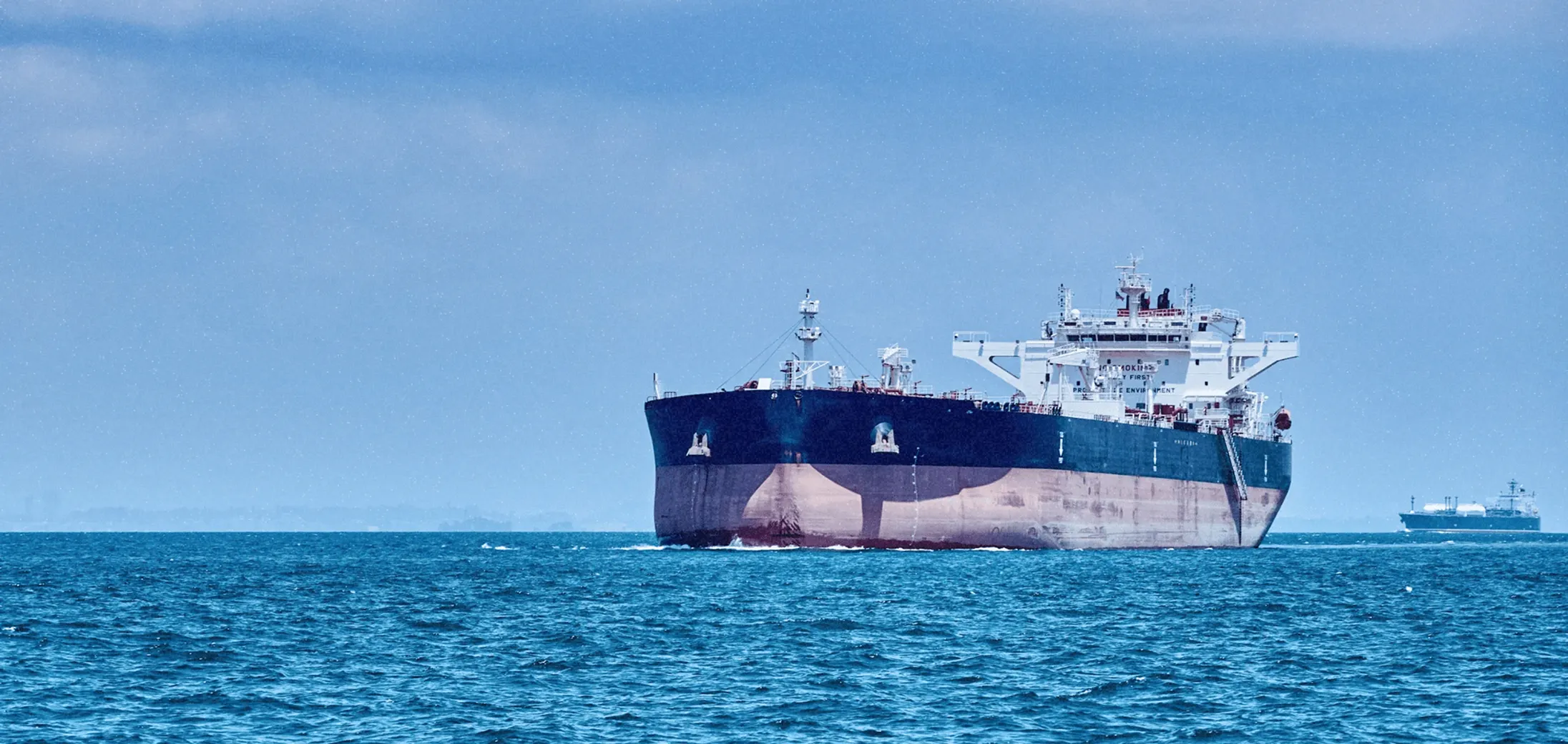 Large cargo ship sailing on a calm blue sea with another ship in the background.