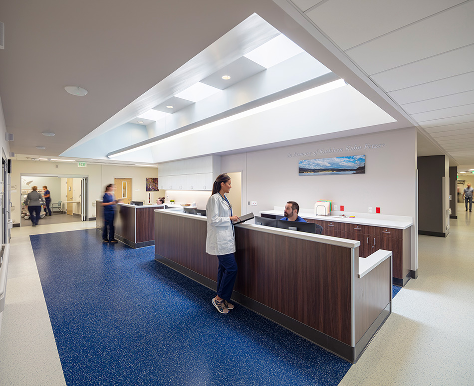 Adventist Health UVMC Ukiah Valley ED Expansion & ICU Addition, Ukiah, CA: Healthcare renovation, tenant improvement and new construction by Herrero Builders in an occupied environment, with Lionakis. Interior view of a nurses station with a dark wood counter and skylight above.
