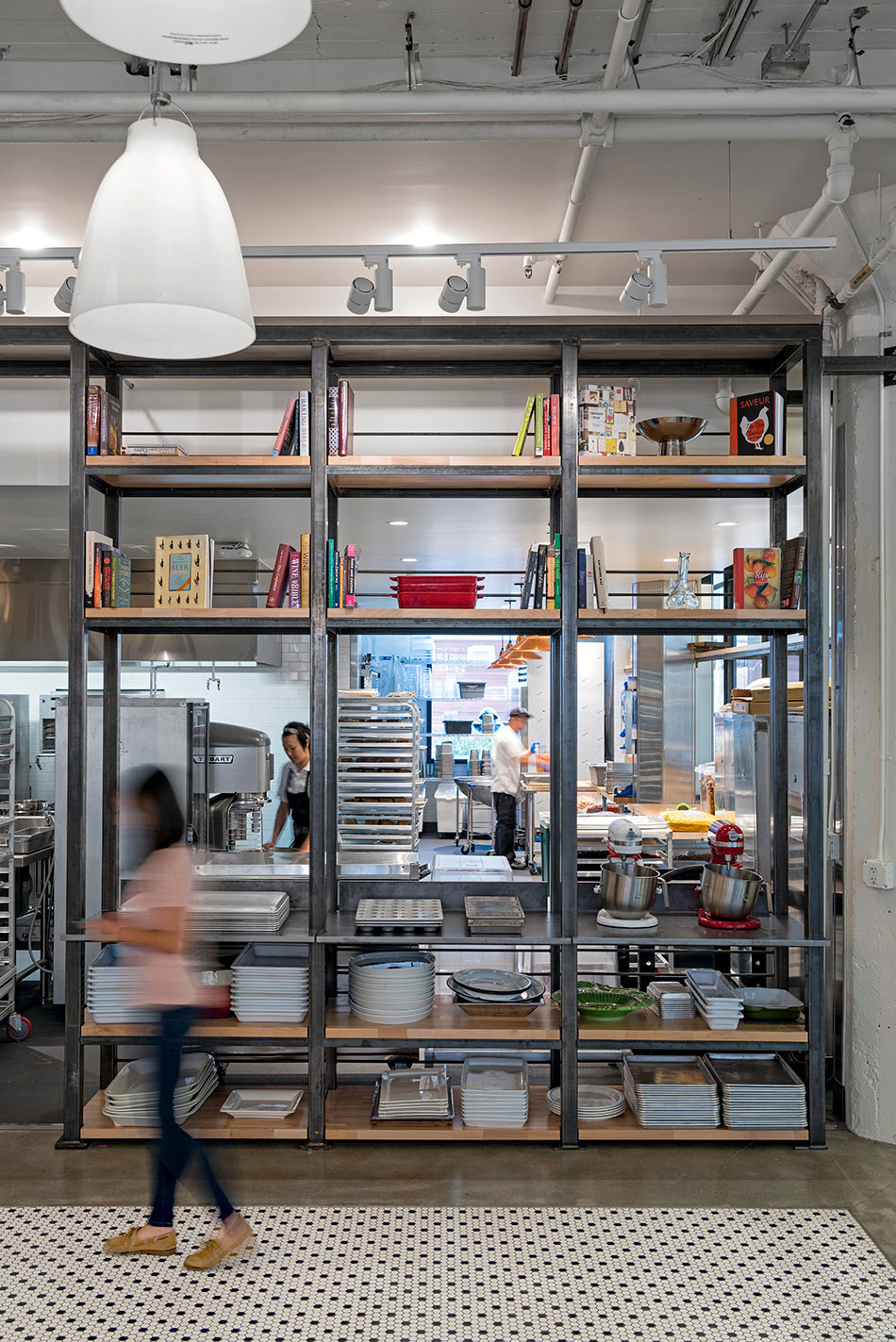 Airbnb Dining Commons & Commercial Kitchen, San Francisco, CA: Commercial & Retail renovation and tenant improvement by Herrero Builders with significant demolition, with WRNS Studio. Interior view of a commercial kitchen behind a steel shelving unit with cookbooks and pans.