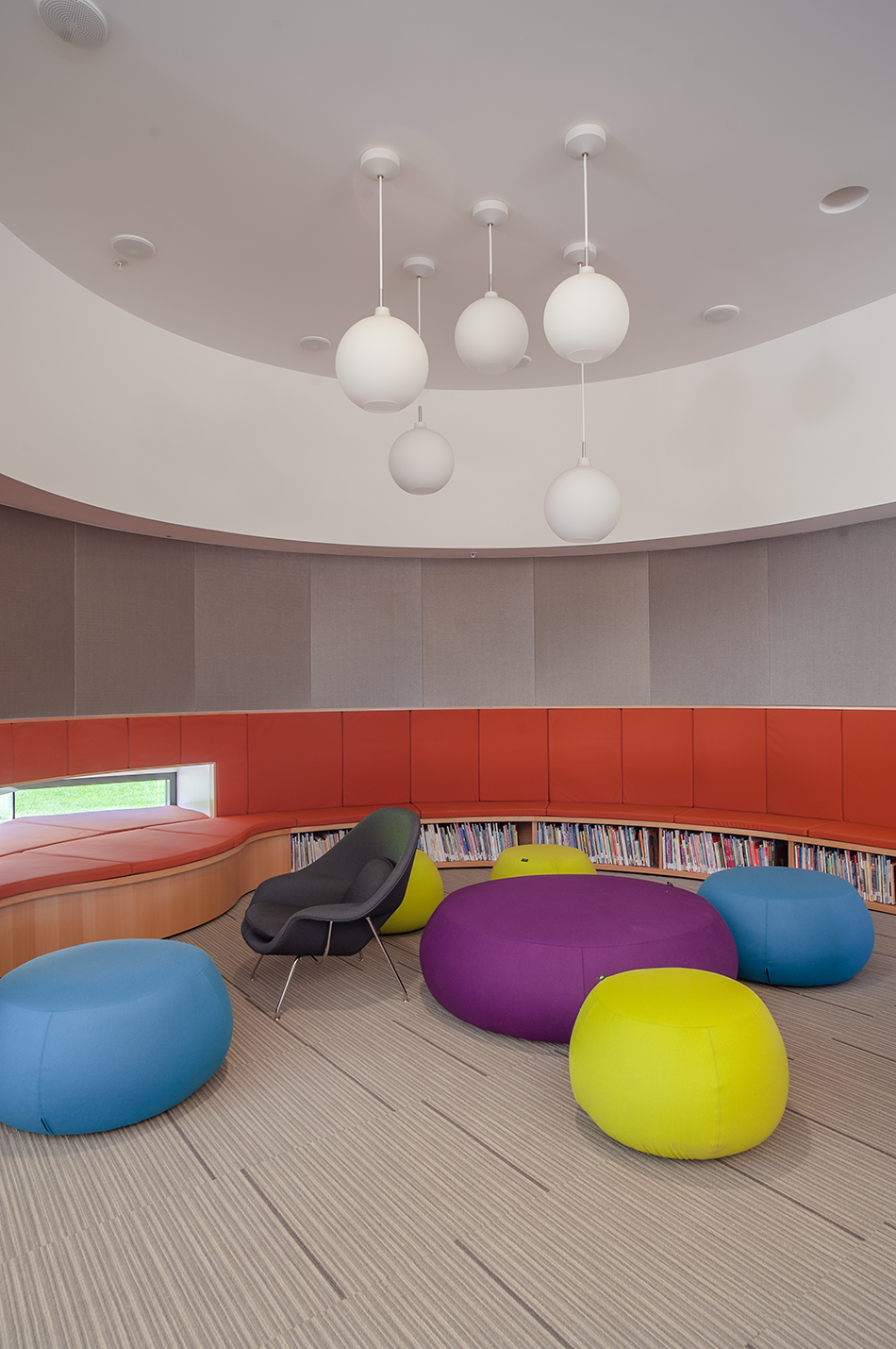 Sacred Heart Schools Atherton Lower & Middle School, Atherton, CA: Education new construction by Herrero Builders on a LEED Gold net zero energy campus, with WRNS Studio. Interior view of a curved reading nook with orange built-in seating, round pendant lights and bright pouf cushions.