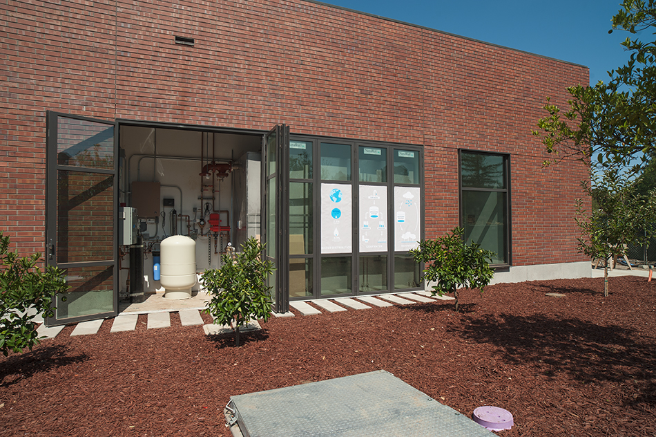 Sacred Heart Schools Atherton Lower & Middle School, Atherton, CA: Education new construction by Herrero Builders on a LEED Gold net zero energy campus, with WRNS Studio. Detail of a brick building with a folding glass door opening onto visible water treatment equipment.