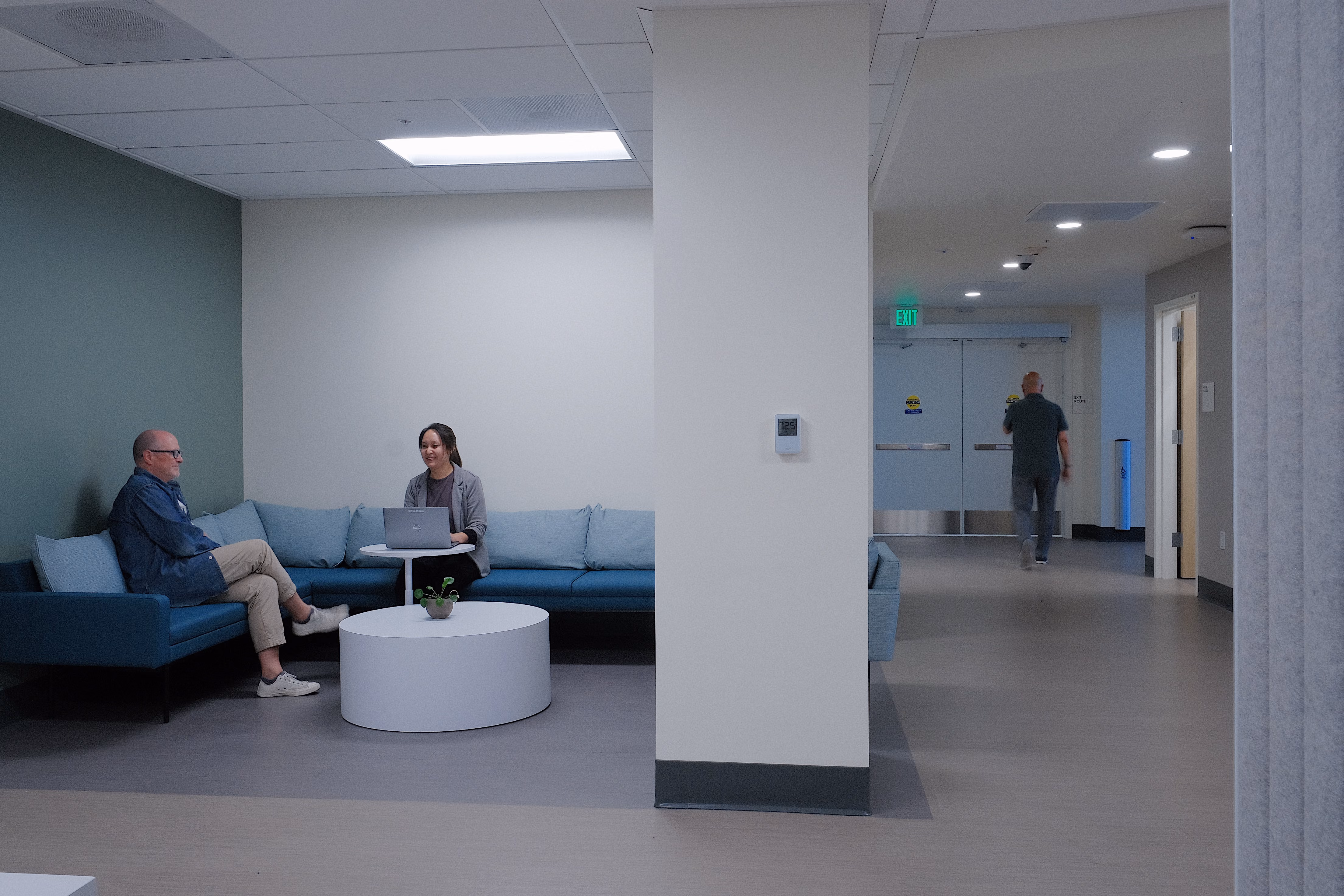 Sutter Health ABSMC Graduate Medical Education (GME), Oakland, Berkeley, CA: Healthcare renovation by Herrero Builders in an occupied hospital, with HOK. Interior view of a seating nook with a blue sofa, round table and two people talking.