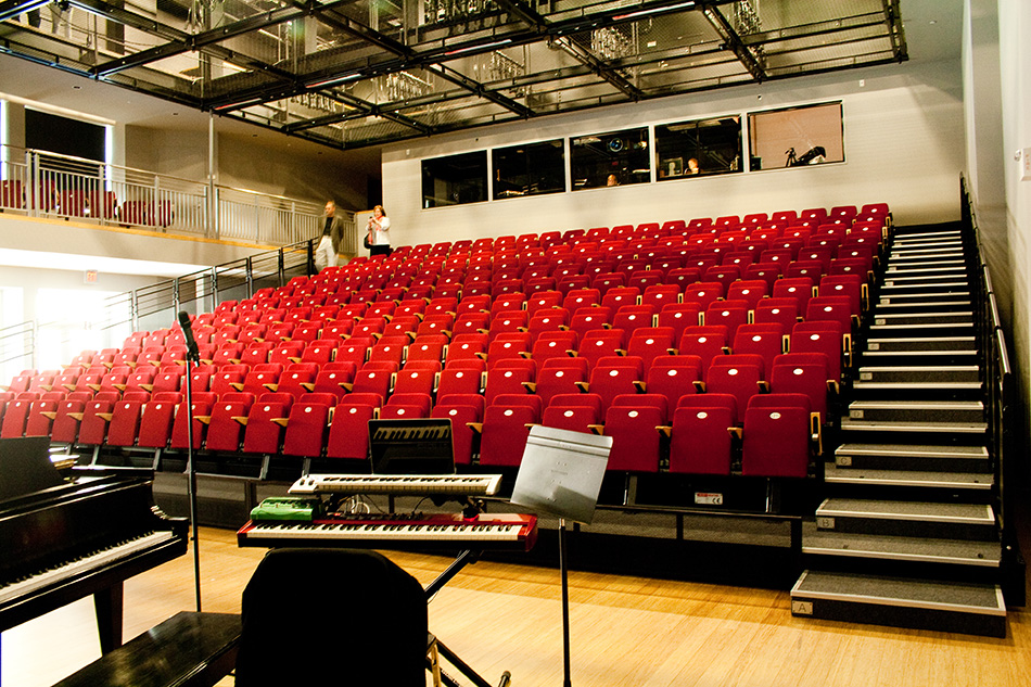 Drew School New Assembly Wing, San Francisco, CA: Education new construction by Herrero Builders with LEED Gold sustainable design, with ROMA Design Group. Interior view of the performance hall with red tiered seating and a stage.