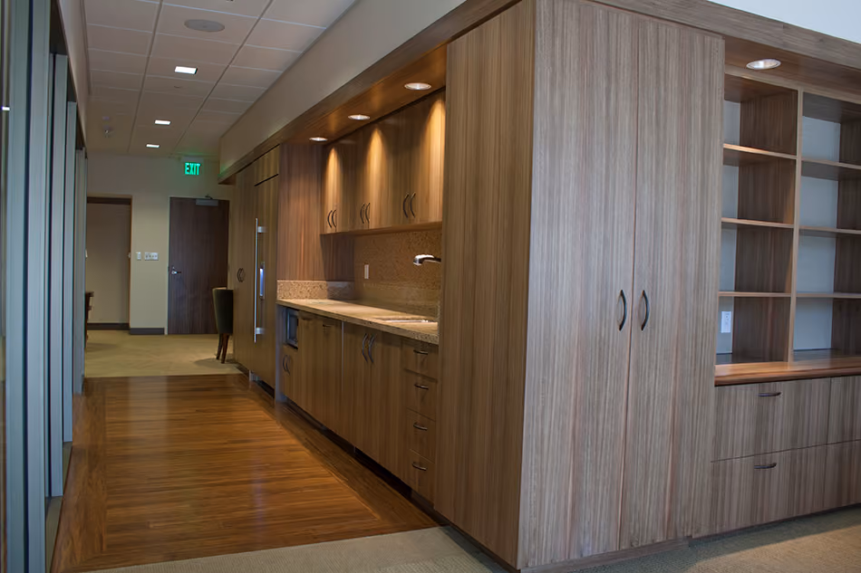 Sutter Health PAMF Burlingame Medical Office Building, Burlingame, CA: Healthcare Tenant Improvements by Herrero Builders under Integrated Project Delivery, with Hawley Peterson Snyder. Detail of built-in wood cabinetry with a counter and open shelving along a hardwood-floored hallway.