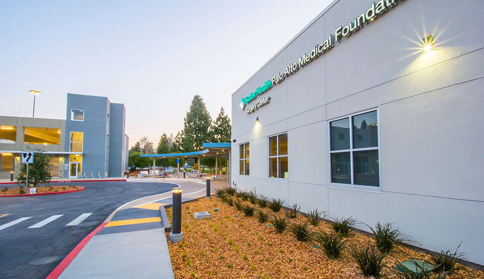 Sutter Health PAMF Fremont Ambulatory Surgery Center & Parking Garage, Fremont, CA: Healthcare New Construction by Herrero Builders in an occupied healthcare environment, with Boulder Architects. Exterior view of the gray surgery center facade with a lit wall sign and the parking structure.