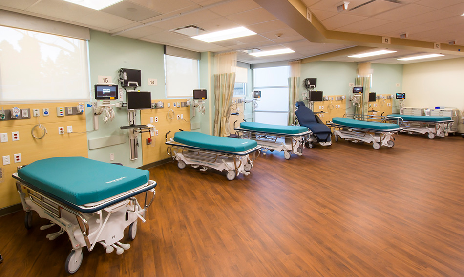 Sutter Health PAMF Fremont Ambulatory Surgery Center & Parking Garage, Fremont, CA: Healthcare New Construction by Herrero Builders in an occupied healthcare environment, with Boulder Architects. Interior view of a recovery bay with teal gurneys, wall-mounted monitors and a wood-look floor.