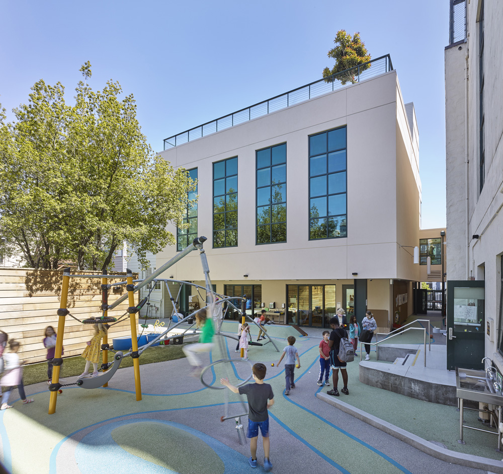 San Francisco Day School School Addition and Staff Housing, San Francisco, CA: Education new construction by Herrero Builders under Integrated Project Delivery, with Studio Bondy. Exterior view of a courtyard playground with climbing structures and children below the white building.