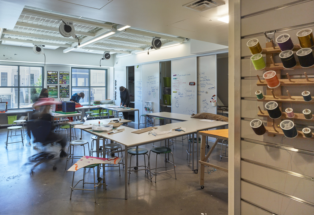 San Francisco Day School School Addition and Staff Housing, San Francisco, CA: Education new construction by Herrero Builders under Integrated Project Delivery, with Studio Bondy. Interior view of a maker studio with long white worktables, stools and a pegboard of thread spools.