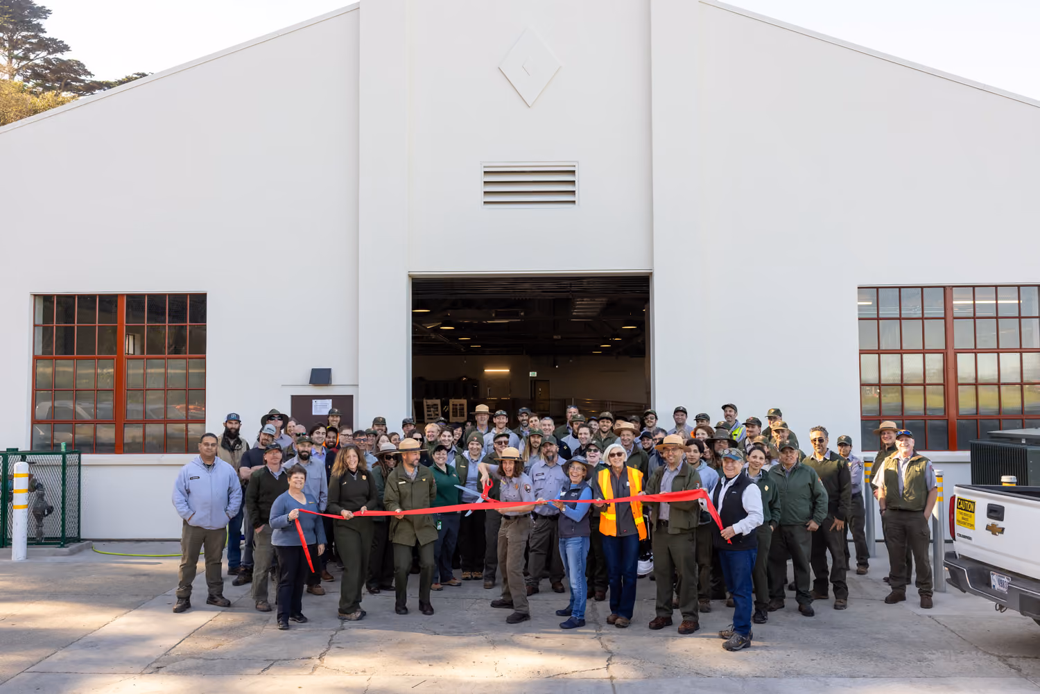 National Park Service Crissy Field Hangar Rehabilitation (Presidio Building 643), San Francisco, CA: Historic renovation by Herrero Builders using Lean construction, with Siegel & Strain Architects. Exterior view of the hangar's open bay door with a group gathered for a ribbon cutting.