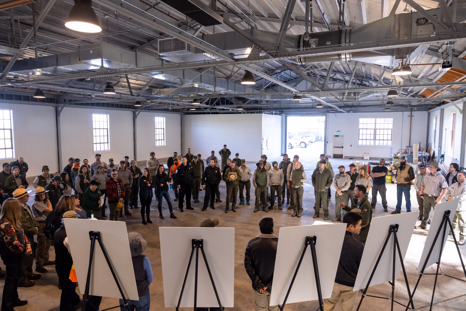 National Park Service Crissy Field Hangar Rehabilitation (Presidio Building 643), San Francisco, CA: Historic renovation by Herrero Builders using Lean construction, with Siegel & Strain Architects. Interior view of the hangar bay with steel trusses and a gathering around easels.