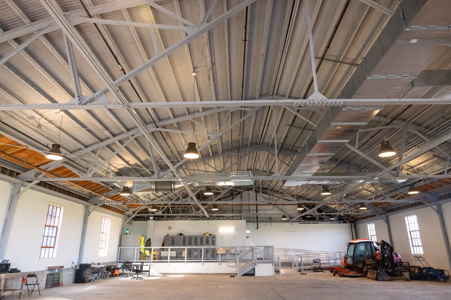 National Park Service Crissy Field Hangar Rehabilitation (Presidio Building 643), San Francisco, CA: Historic renovation by Herrero Builders using Lean construction, with Siegel & Strain Architects. Interior view of the rehabilitated hangar with steel roof trusses, pendant lights and tall windows.