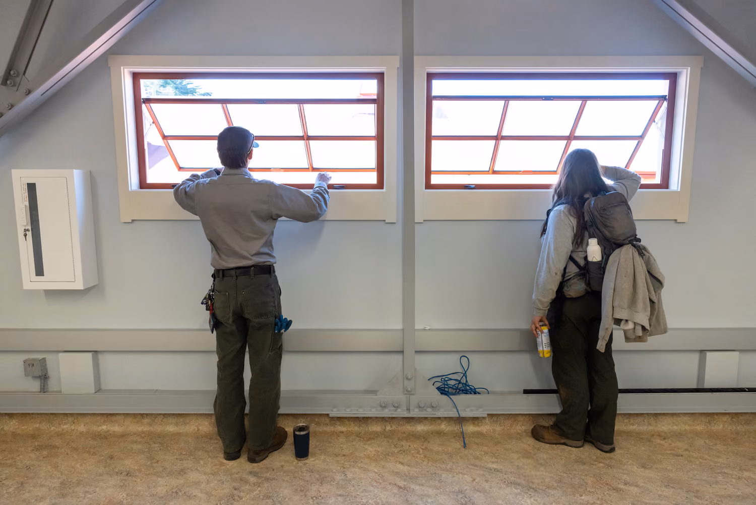National Park Service Crissy Field Hangar Rehabilitation (Presidio Building 643), San Francisco, CA: Historic renovation by Herrero Builders using Lean construction, with Siegel & Strain Architects. Detail of two people at red-framed operable windows beneath a trussed ceiling.