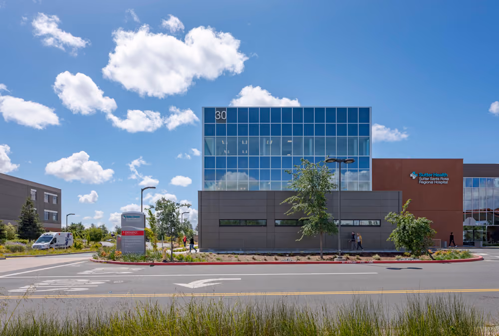 Sutter Health Santa Rosa Regional Hospital Expansion, Santa Rosa, CA: Healthcare New Construction by Herrero Builders under Integrated Project Delivery with Lean construction, with Stantec. Exterior view of the glass tower, dark gray base and entrance canopy seen from the street.