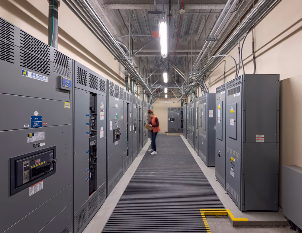 Sutter Health Santa Rosa Regional Hospital Expansion, Santa Rosa, CA: Healthcare New Construction by Herrero Builders under Integrated Project Delivery with Lean construction, with Stantec. Interior view of an electrical room with rows of gray switchgear cabinets and a grated walkway.
