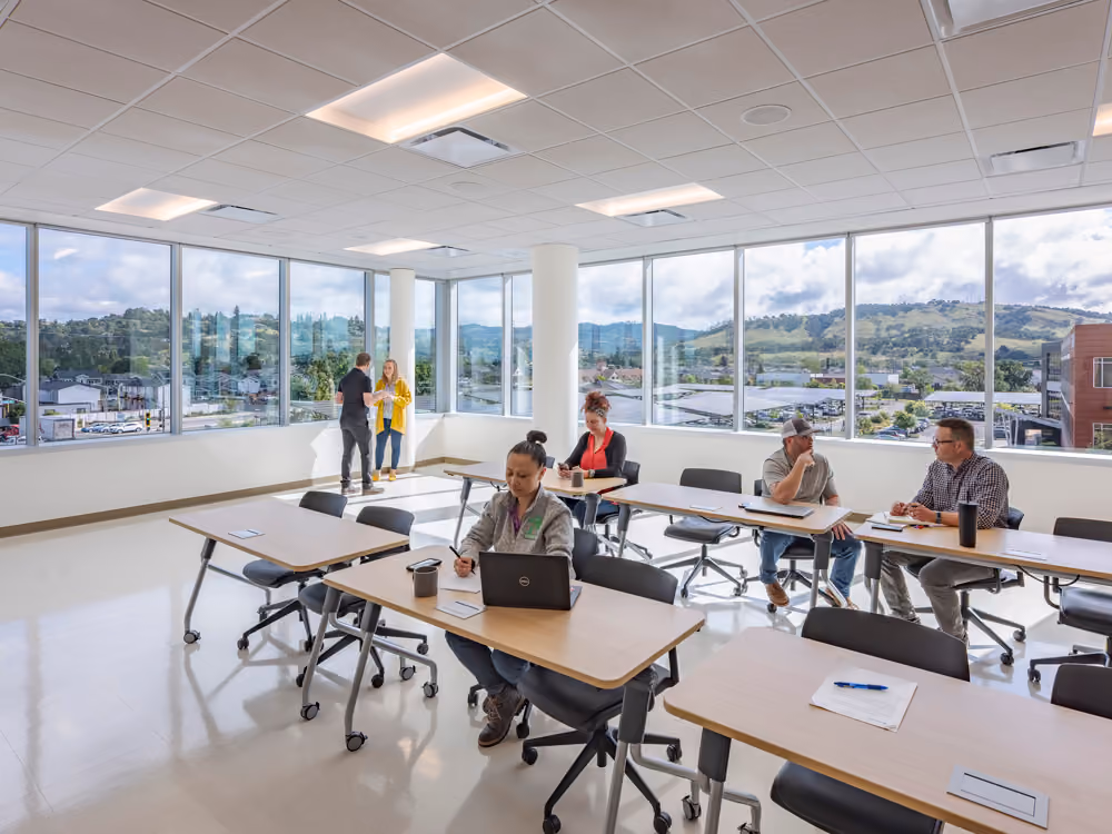 Sutter Health Santa Rosa Regional Hospital Expansion, Santa Rosa, CA: Healthcare New Construction by Herrero Builders under Integrated Project Delivery with Lean construction, with Stantec. Interior view of a training room with tables, laptops and a wall of windows facing hills.