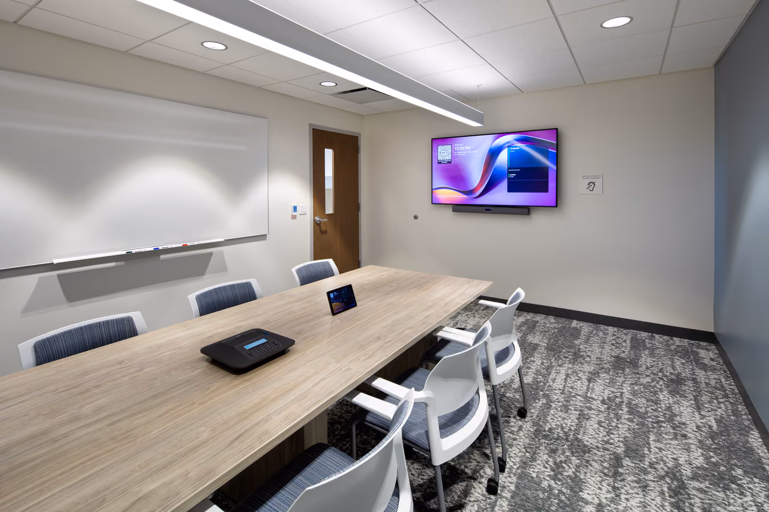 Sutter Health Monteagle Multispecialty Center, San Francisco: Healthcare multi-floor tenant improvement by Herrero Builders occupied during construction, with Polytech Architects and HED. Interior view of a conference room with a wood table, white chairs and a wall-mounted display.
