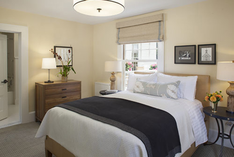 The Presidio Trust Funston House, San Francisco, CA: Hospitality and Historic renovation by Herrero Builders preserving a historic officer's home, with Architectural Resource Group. Interior view of a guest bedroom with a navy throw, wood dresser and a shaded window.