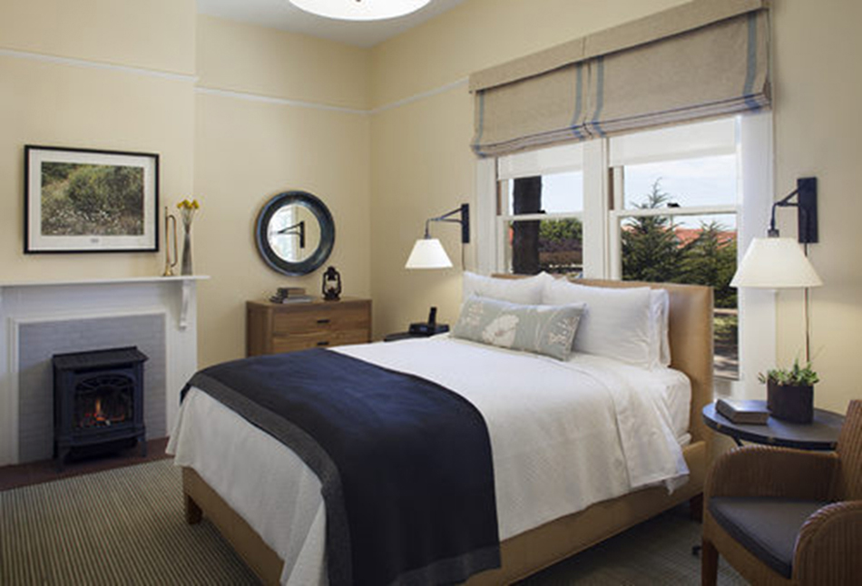 The Presidio Trust Funston House, San Francisco, CA: Hospitality and Historic renovation by Herrero Builders preserving a historic officer's home, with Architectural Resource Group. Interior view of a guest bedroom with a gas fireplace stove and a round mirror.