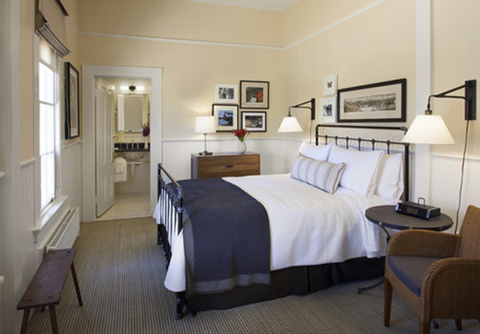 The Presidio Trust Funston House, San Francisco, CA: Hospitality and Historic renovation by Herrero Builders preserving a historic officer's home, with Architectural Resource Group. Interior view of a guest bedroom with an iron bed, wicker chair and an en-suite bath beyond.