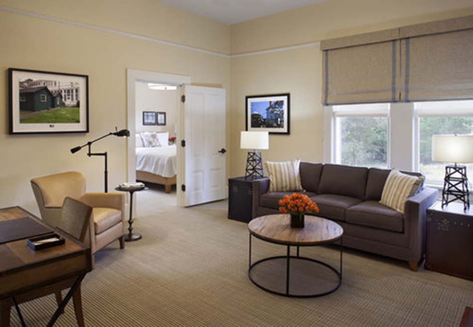 The Presidio Trust Funston House, San Francisco, CA: Hospitality and Historic renovation by Herrero Builders preserving a historic officer's home, with Architectural Resource Group. Interior view of a suite sitting area with a sofa and desk and a bedroom through an open door.