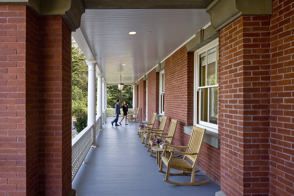The Presidio Trust Inn at the Presidio, San Francisco, CA: Hospitality and Historic renovation by Herrero Builders preserving a National Historic Landmark, with Architectural Resources Group. Exterior view of a covered brick porch with white columns and rocking chairs along the veranda.